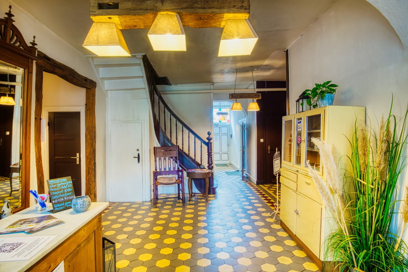 Eingangsbereich mit gelb-grauen Wabenfliesen, Holztreppe und hellem Schrank.