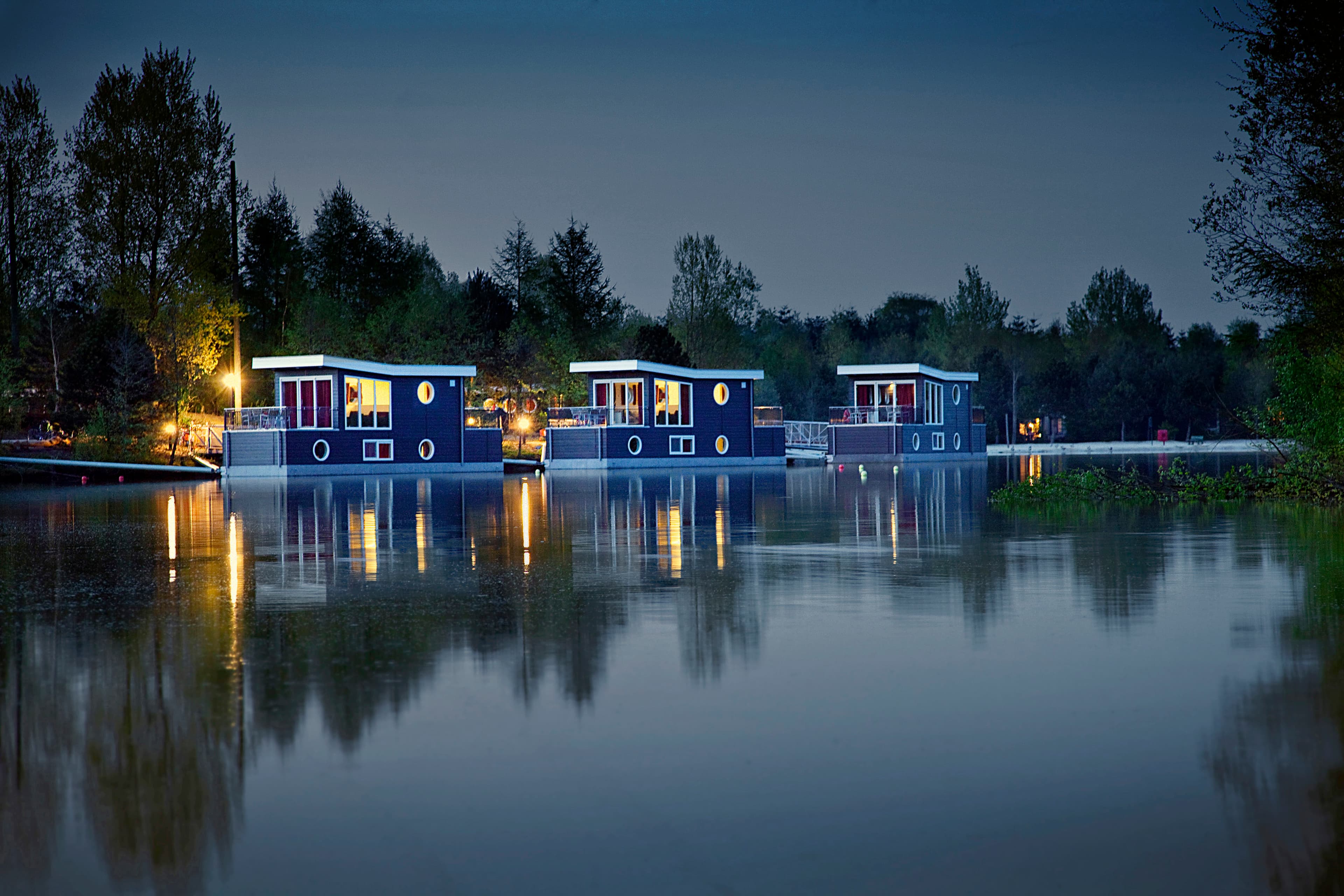 Moderne Hausboote im Center Parcs Bispinger Heide bei Abenddämmerung auf stiller Wasseroberfläche.