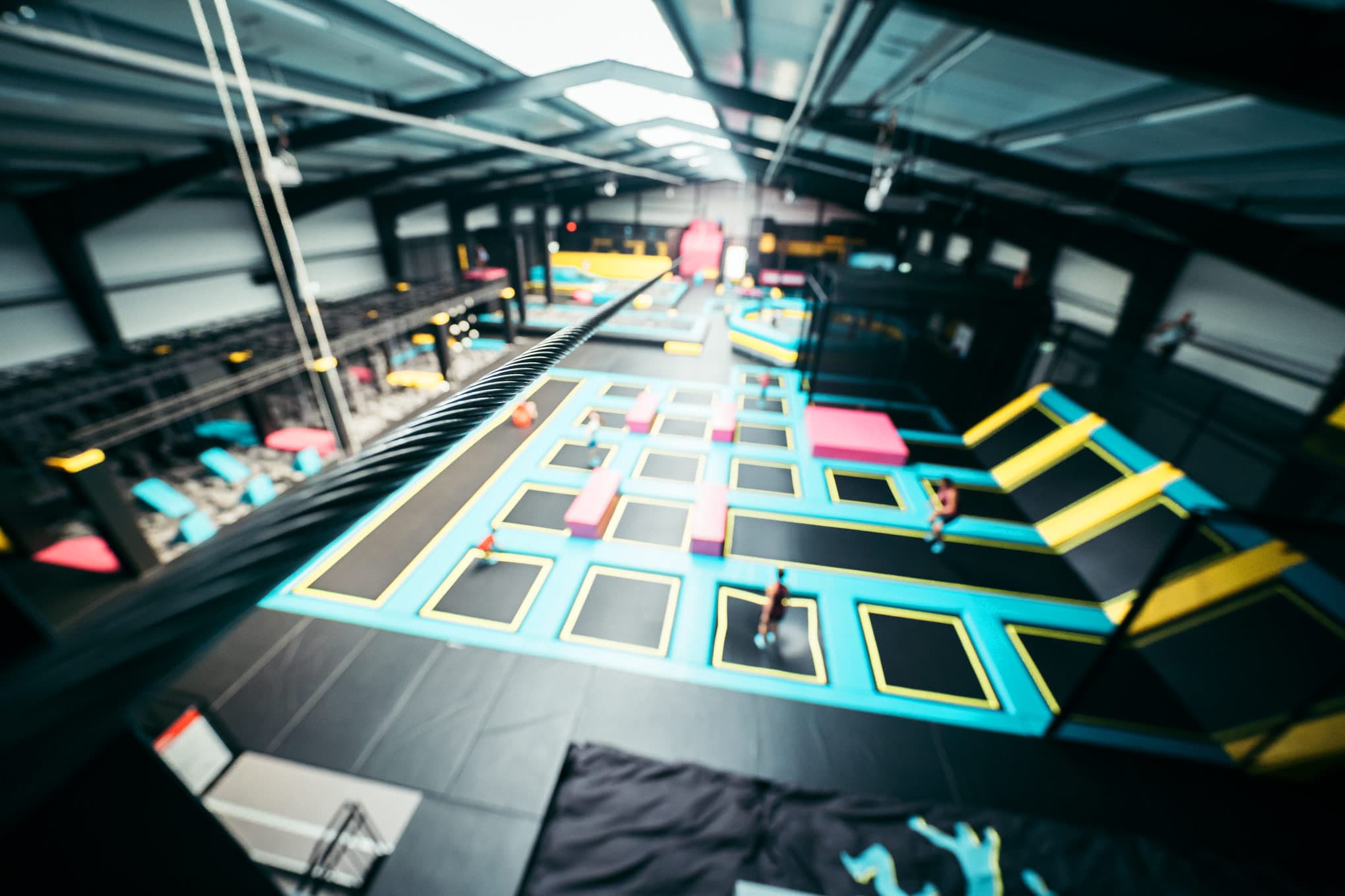 Das Bild zeigt eine große, helle Halle mit verschiedenen Trampolinen in leuchtenden Farben, die zur sportlichen Nutzung angeordnet sind. Bewegung im Hintergrund deutet auf aktive Besucher hin.The picture shows a large, bright hall with various trampolines in bright colors arranged for sports use. Movement in the background indicates active visitors.Billedet viser en stor, lys hal med forskellige trampoliner i stærke farver, der er opstillet til sportslig brug. Bevægelse i baggrunden indikerer aktive besøgende.De foto toont een grote, lichte hal met verschillende trampolines in felle kleuren, opgesteld voor sportief gebruik. Beweging op de achtergrond duidt op actieve bezoekers.
