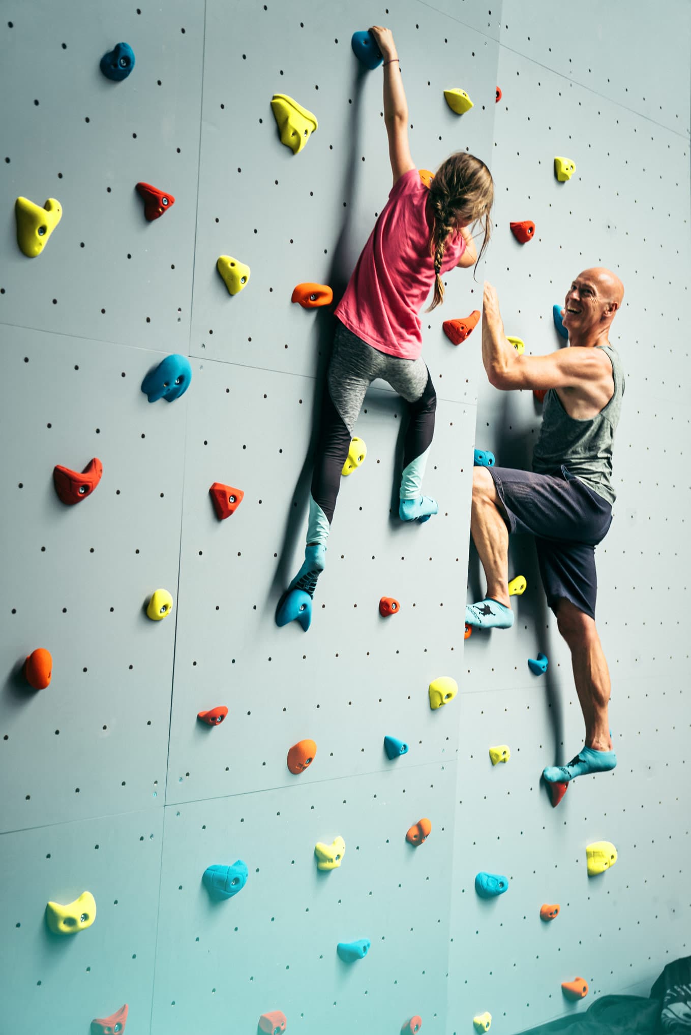 Ein Mädchen und ein Mann klettern an einer bunten Kletterwand, fröhlich und konzentriert.A girl and a man climb on a colorful climbing wall, cheerful and concentrated.En pige og en mand klatrer på en farverig klatrevæg, glade og koncentrerede.Een meisje en een man klimmen vrolijk en geconcentreerd op een kleurrijke klimwand.