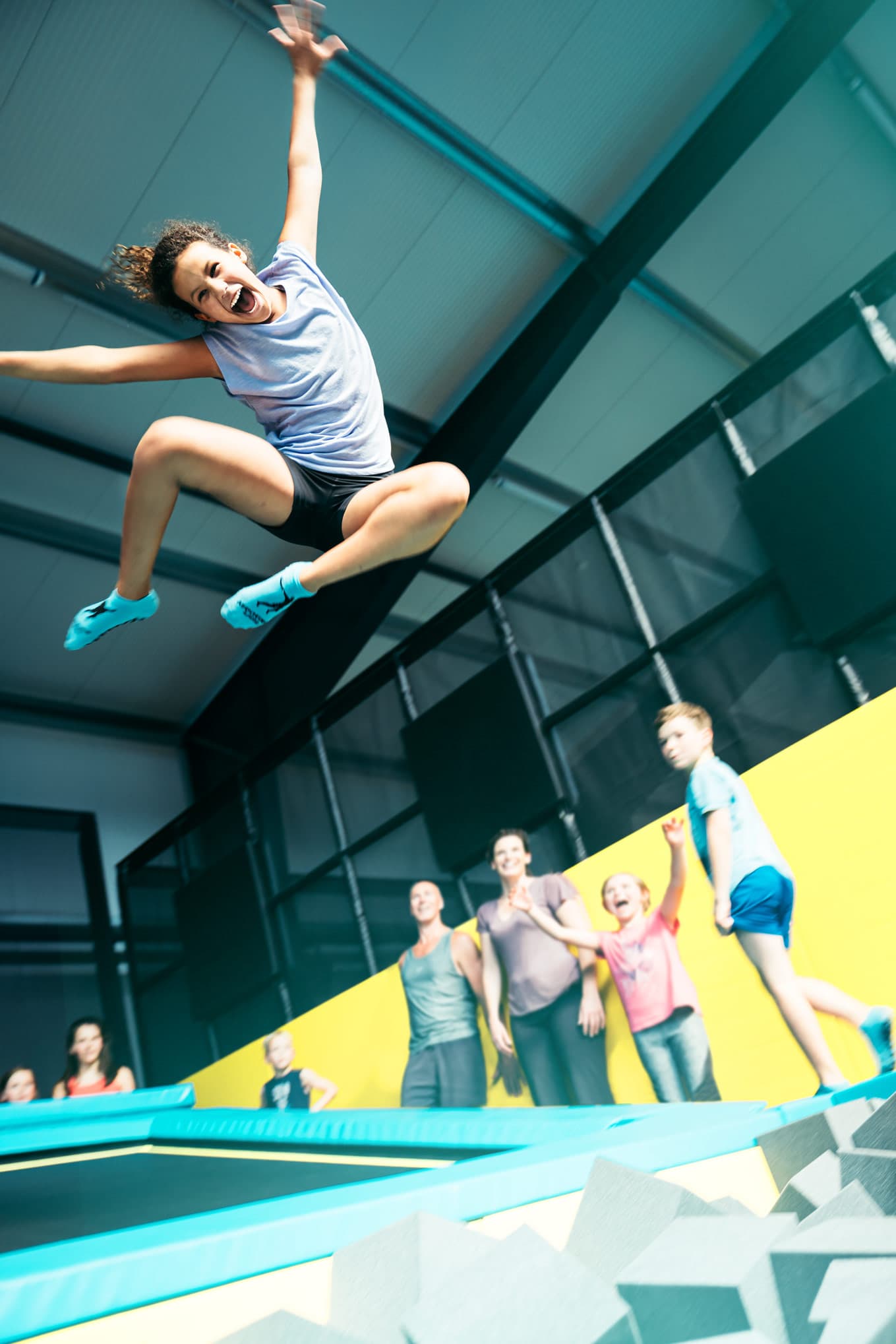 Eine Frau springt freudestrahlend auf einem Trampolin, während im Hintergrund mehrere Personen zusehen.A woman jumps on a trampoline, beaming with joy, while several people watch in the background.En kvinde hopper på en trampolin og stråler af glæde, mens flere mennesker ser til i baggrunden.Een vrouw springt op een trampoline, stralend van vreugde, terwijl verschillende mensen op de achtergrond toekijken.