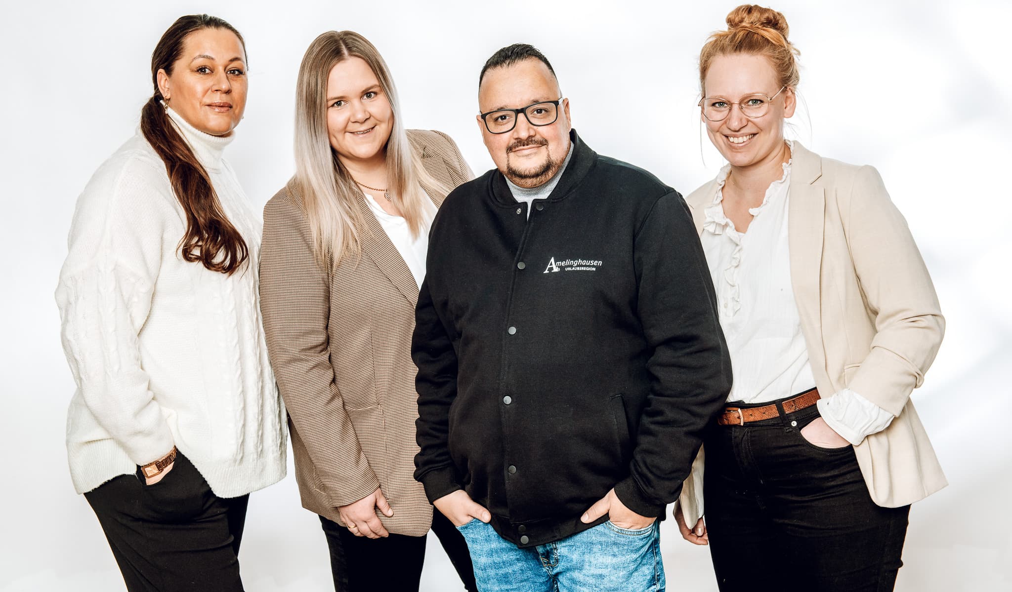 Vier freundlich lächelnde Menschen in Business-Kleidung vor weißem Hintergrund.