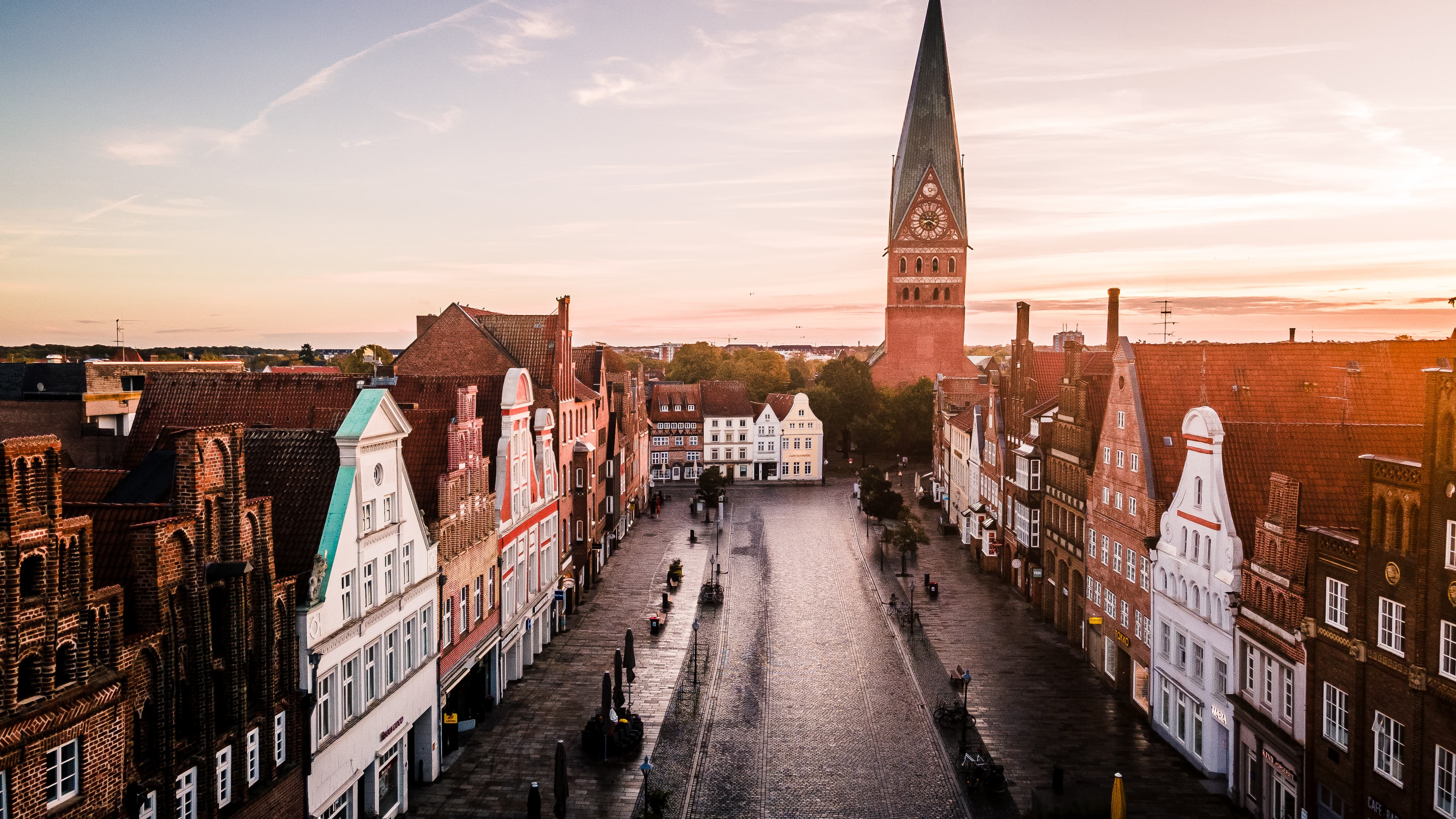 Platz Am Sande mit historischen Giebelhäusern und der St. Johanniskirche im Sonnenlicht.