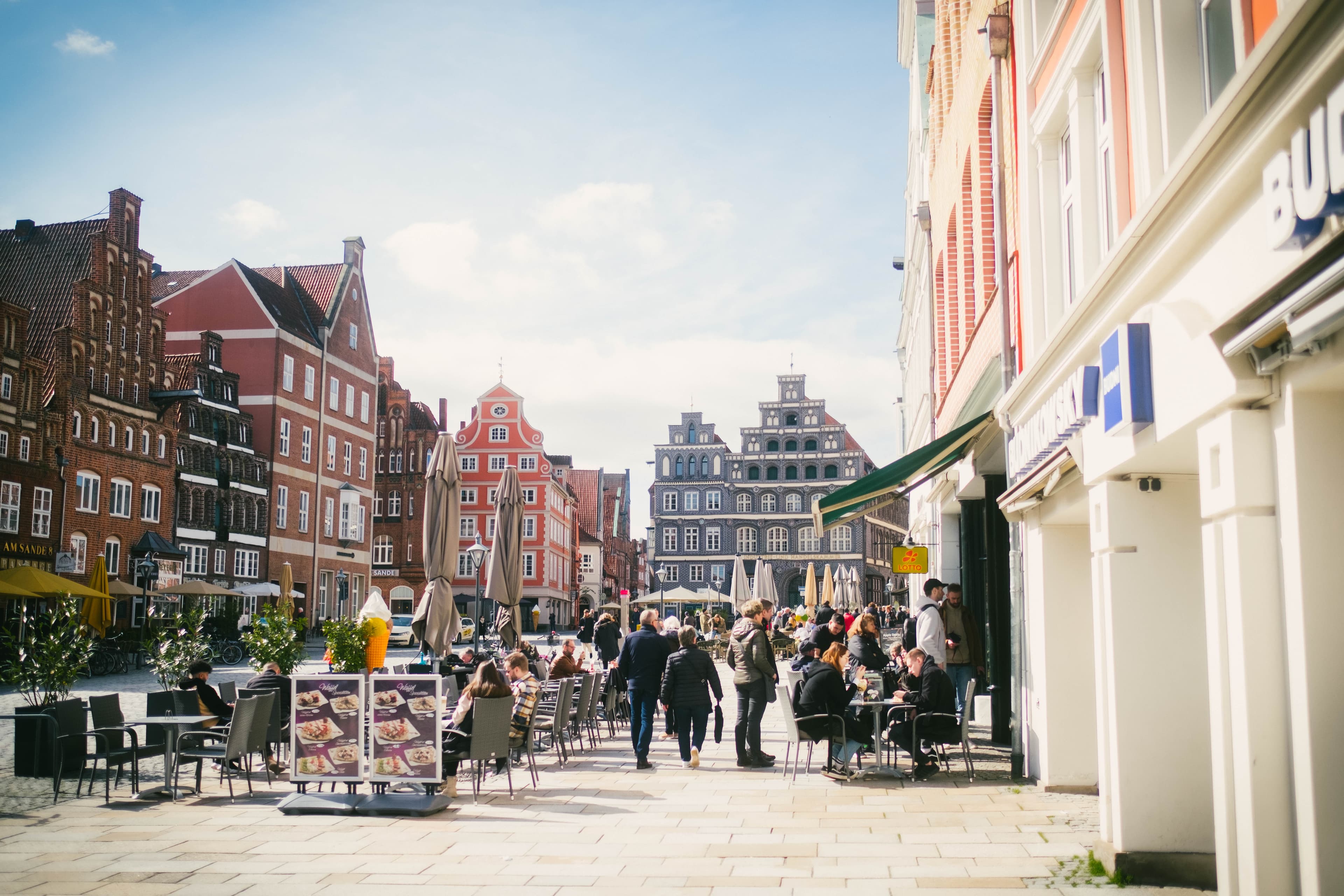 Platz Am Sande in Lüneburg mit historischen Backsteinhäusern, Cafés und Menschen im Sonnenschein.