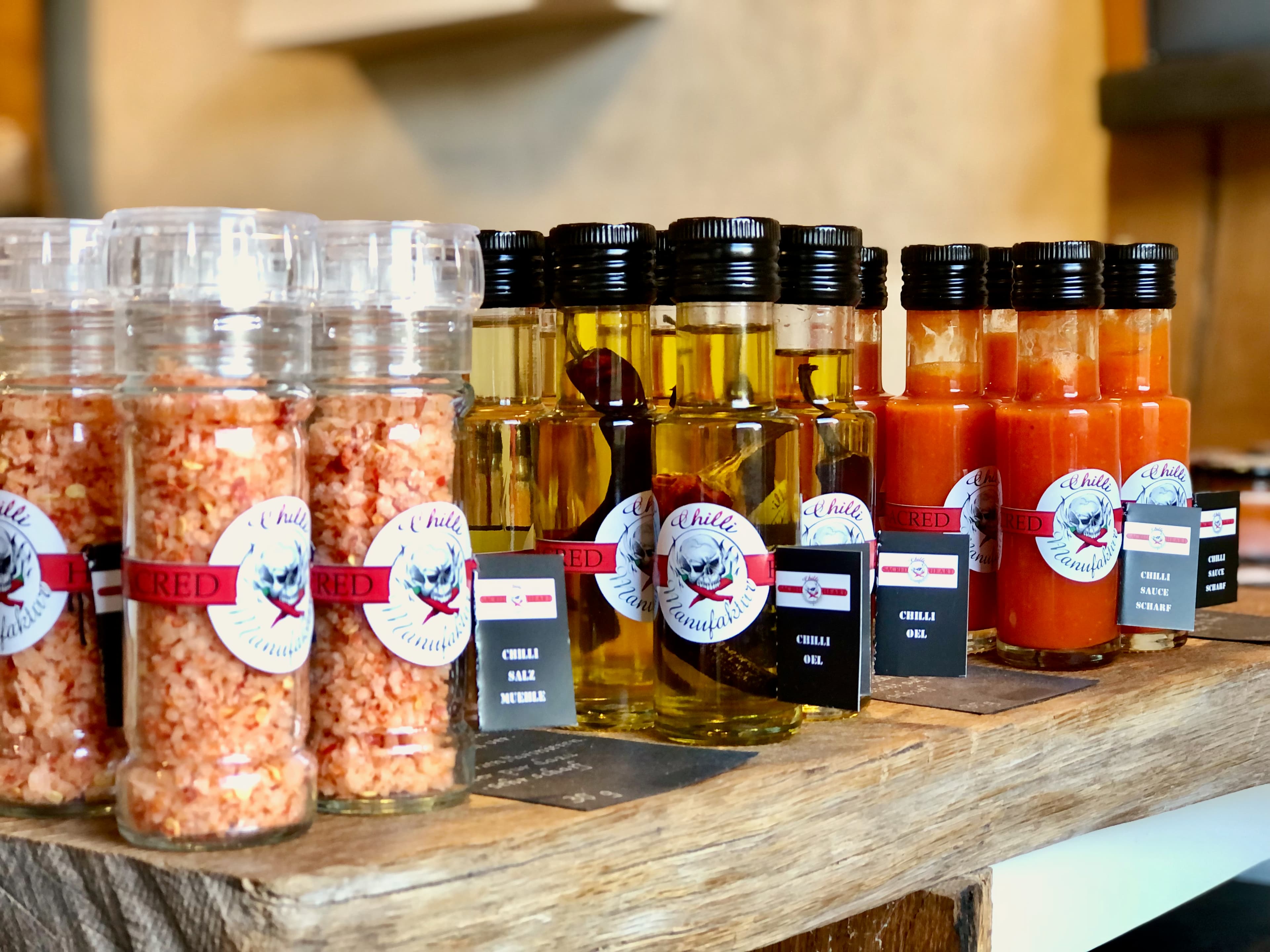 Das Bild zeigt Chili Salzmühlen, Chiliölflaschen und Chilisaucen in der Flasche auf einem Eichentisch im Hofladen stehend Chilli Manufaktur Susanne Menke Lüneburger