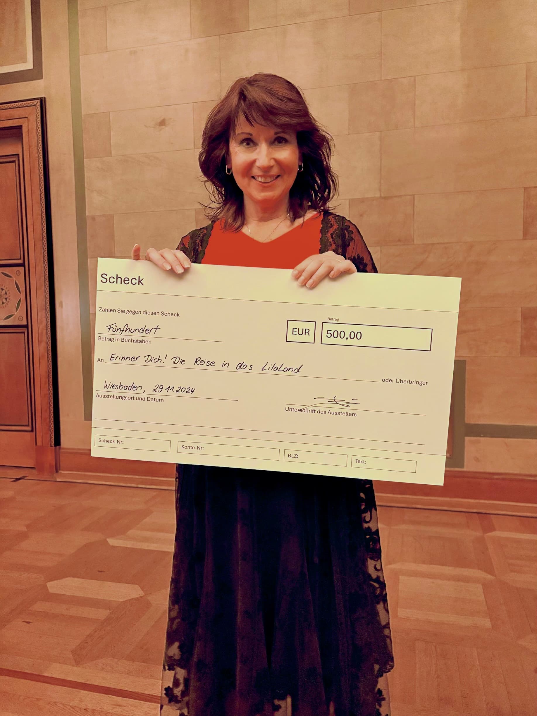 eine frau hält einen grossen cheque in der hand und lächelt in die kamera