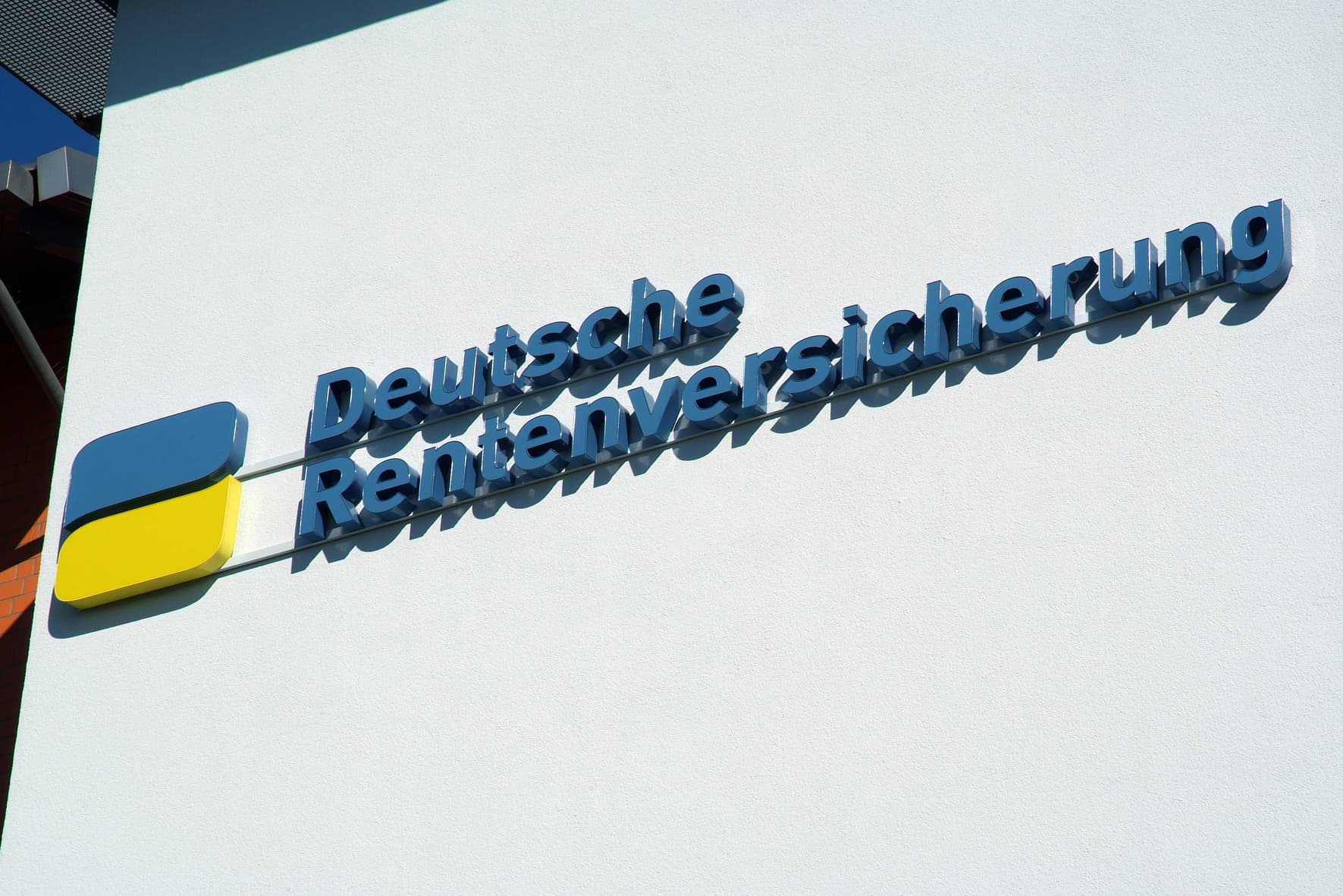 Das Bild zeigt ein blau-gelbes Logo mit dem Schriftzug "Deutsche Rentenversicherung" an einer weißen Wand.