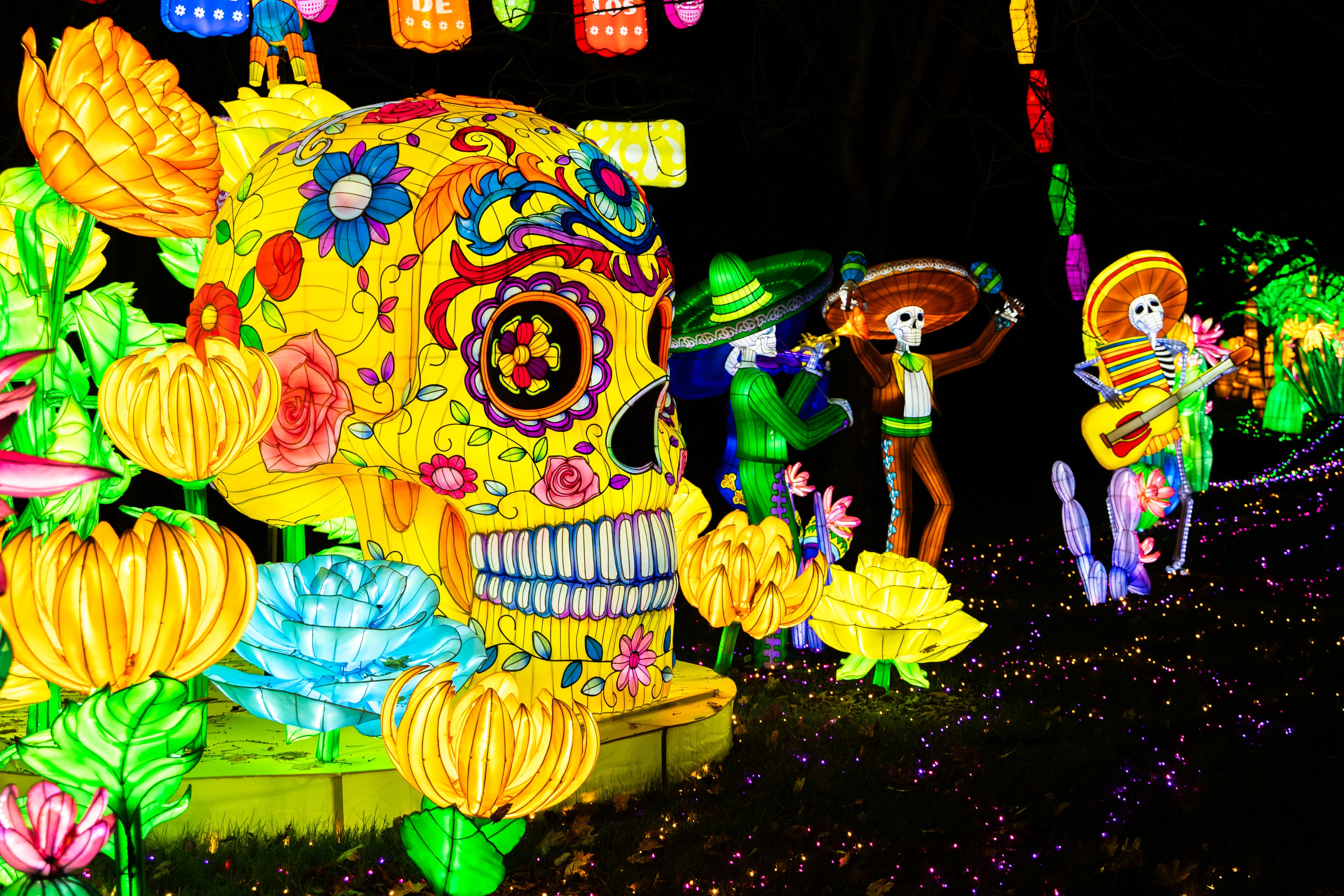 ein leuchtender übergroßer totenkopf in gelb und bunten farben vor drei erleuchteten skeletten