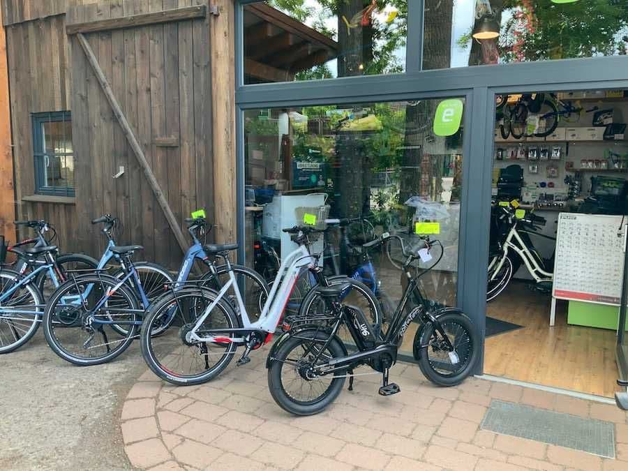 Mehrere Fahrräder sind vor einem modernen Laden mit hölzernem Scheunenflair abgestellt.Electric bikes are arranged outside a shop, showcasing a welcoming display for cycling enthusiasts.
