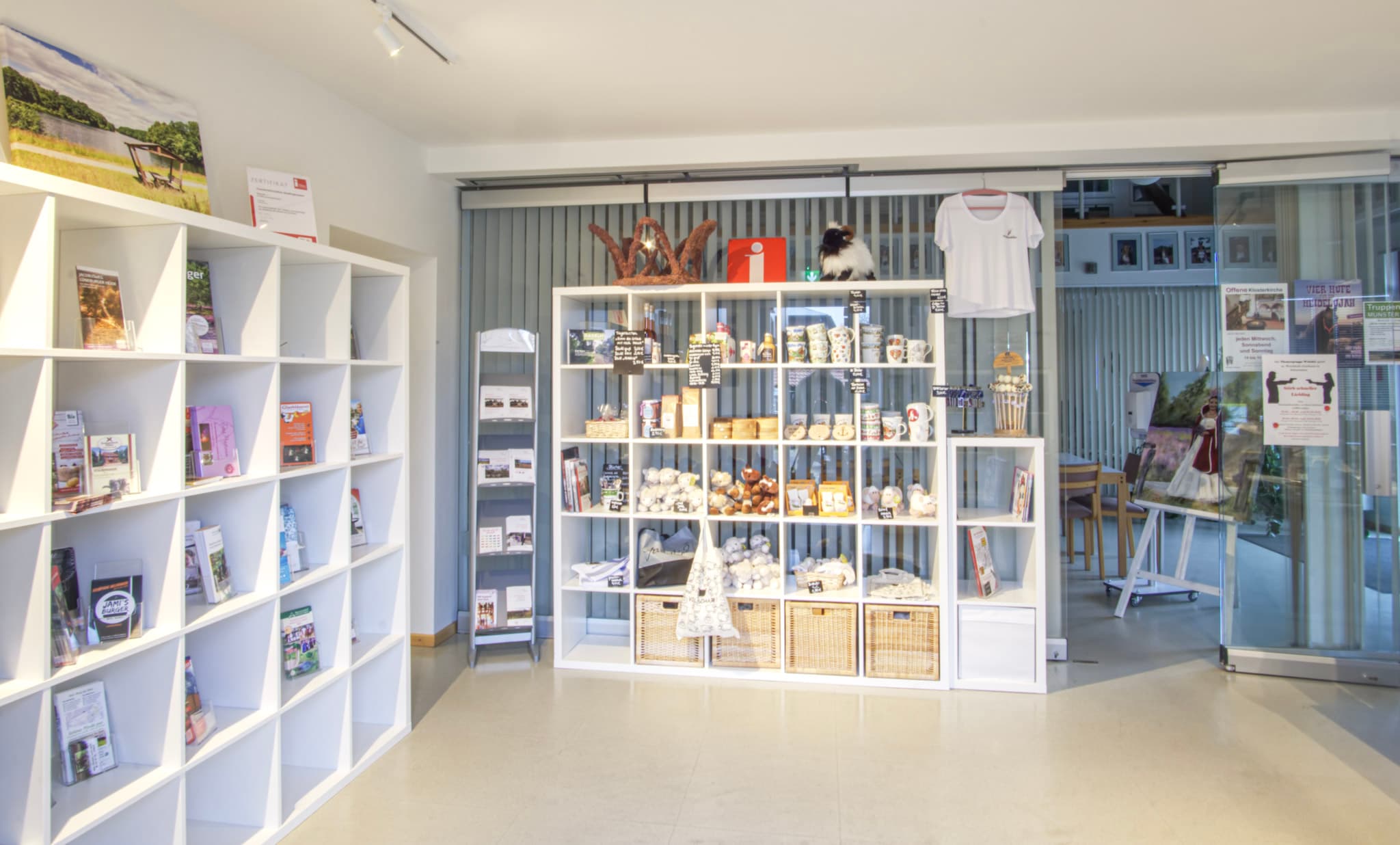 In einem hellen Raum mit modernen, weißen Regalen werden lokale Produkte und Souvenirs stilvoll präsentiert. Ein großes Schiebetor aus Glas im Hintergrund trägt zur offenen und einladenden Atmosphäre bei.